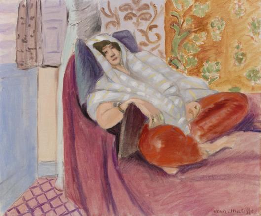 A woman reclines on a violet divan, head veiled in a pale striped cloth, against panels of lilac stripes, tan arabesques, and orange floral pattern; red cushions or trousers glow at her legs and a pink tiled floor appears at lower left, painted by Henri Matisse.