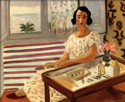 A woman in a white patterned dress sits beside a small glass-topped dressing table with pink flowers, bottles, and hairpins; behind her an open window reveals red balcony stripes, turquoise sea, and a palm, while patterned wallpaper frames the right edge in a warmly lit interior.