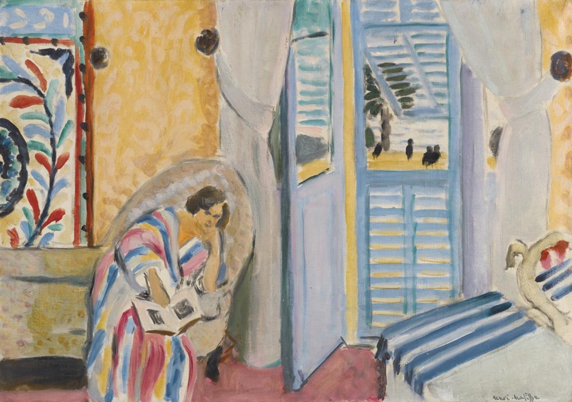 A woman in a pink-yellow-blue striped robe reads in a wicker chair inside a bright room; to the right an open door with light-blue shutters reveals palm and sky, while a floral patterned hanging decorates the left wall and a bed with blue-and-white stripes fills the foreground.