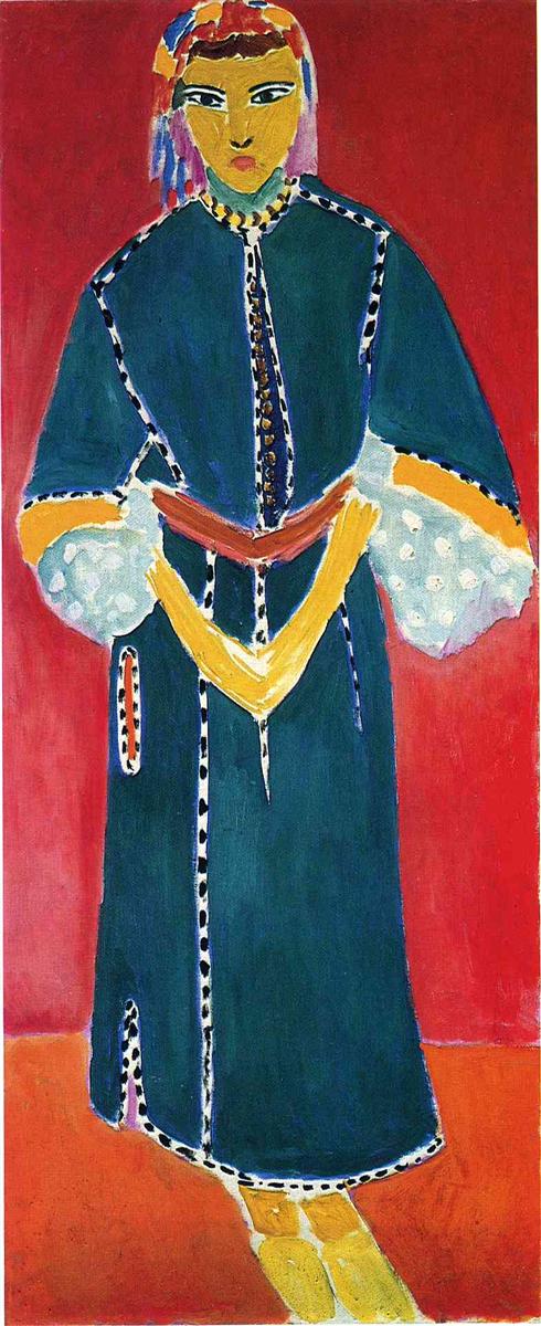 A tall vertical portrait by Henri Matisse showing Zorah standing frontally in a blue-green robe with dotted trim and a red belt, hands folded into a diamond at the waist, set against a flat red wall and ocher floor with a patterned headscarf and simplified facial features.