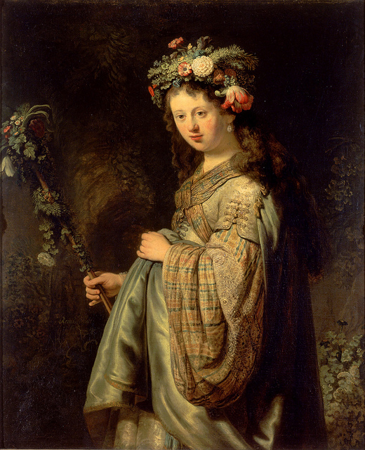 Rembrandt’s “Flora” shows a young woman crowned with flowers holding a blossom-wrapped staff, dressed in embroidered robes and a silvery mantle, softly lit against a dark garden background.