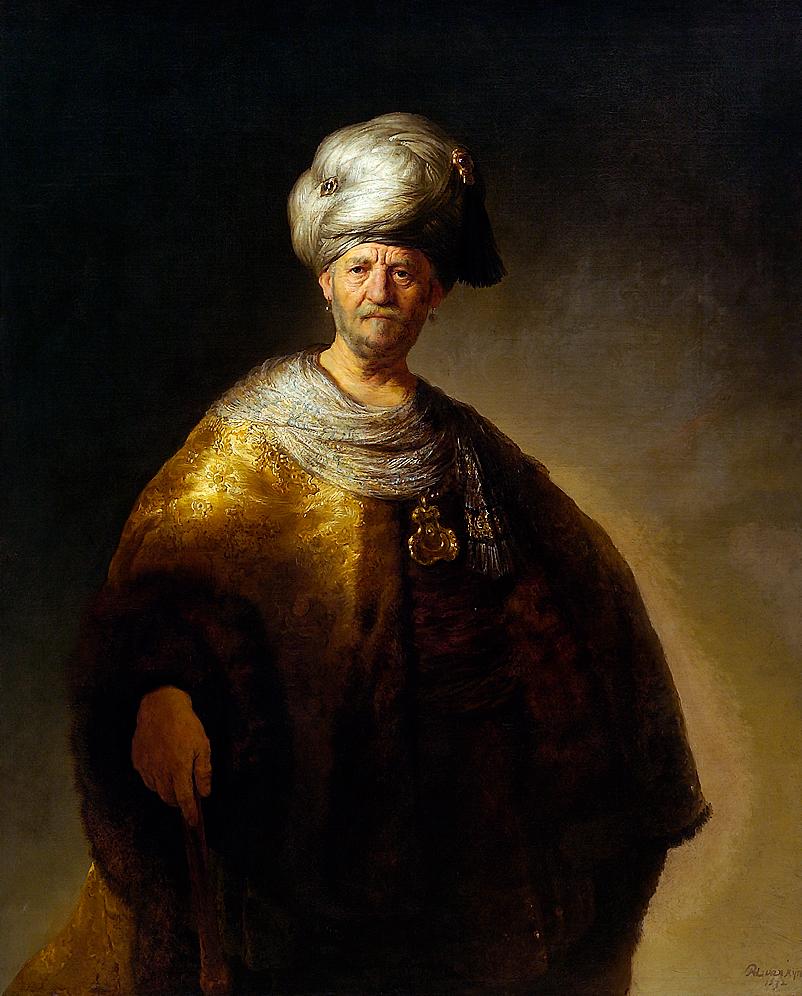 Half-length Rembrandt painting of an older man in a silver turban and golden fur-trimmed robe, illuminated against a dark ground; a jeweled pendant glitters at his chest while his lined face, calm and thoughtful, becomes the focus amid sumptuous fabrics.