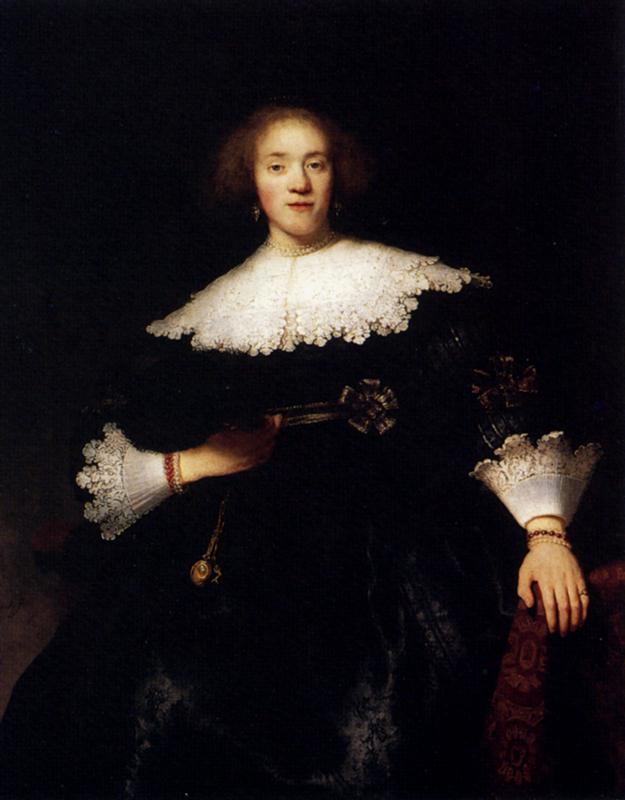 Three-quarter-length portrait of a young woman seated in a dark interior, wearing a broad white lace collar and cuffs, holding a closed fan, with one hand resting on a patterned armrest, softly lit against a dark background.