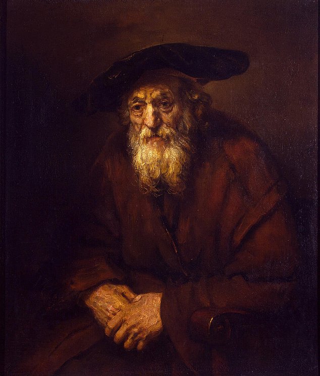 Oil portrait of an elderly Jewish man in a dark cap and reddish-brown cloak, clasping his hands and leaning forward slightly; Rembrandt’s warm light illuminates his lined face and beard against a deep brown background.