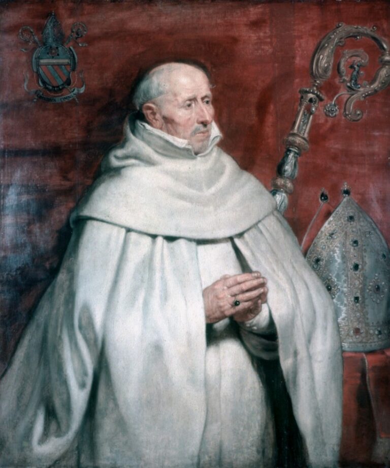 Three-quarter portrait of an abbot in a voluminous white habit before a deep red tapestry, hands clasped in prayer, with a jeweled miter and ornate crozier beside him and an armorial crest at left, painted with restrained light and soft detail.
