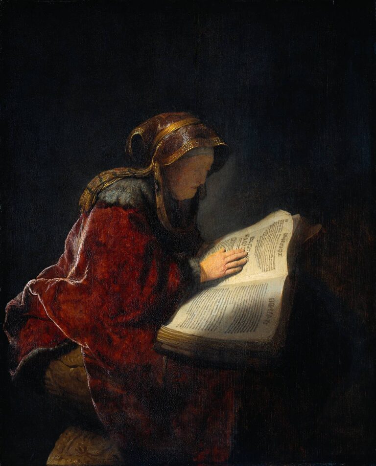 Rembrandt’s 1631 painting of an elderly woman in a fur-lined red mantle and gold-trimmed hood bending over a large open book; soft light illuminates her face, hand, and the page, while the surrounding room recedes into deep shadow.
