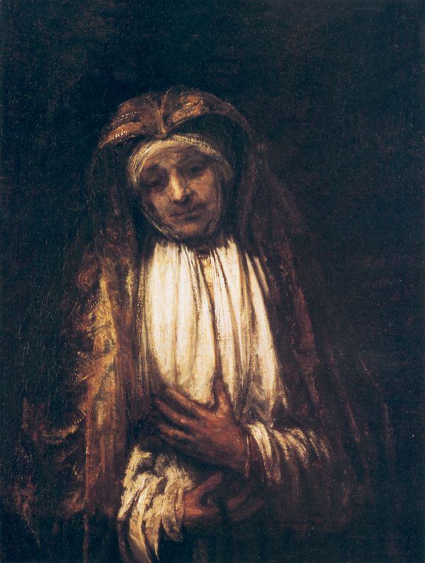 Half-length Rembrandt image of the Virgin Mary in a dark mantle and veil, head bowed with one hand pressed to her chest and the other gathering white linen, softly lit against a deep brown background.