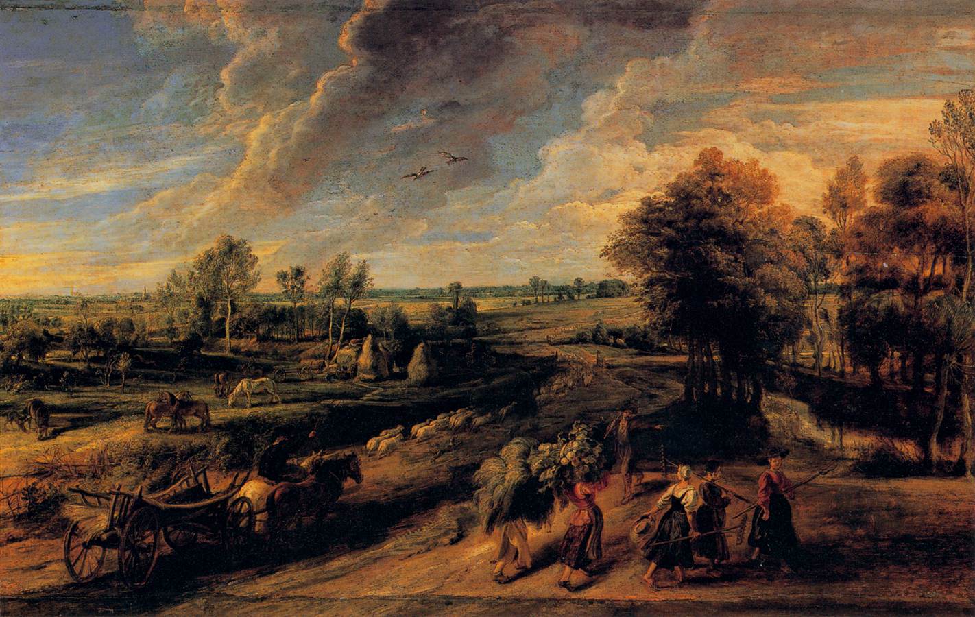 Wide Baroque landscape painting by Peter Paul Rubens showing a Flemish countryside at sunset with a huge cloud-filled sky, distant fields and haystacks, grazing horses and sheep, a horse-drawn cart in the foreground, and a group of farm workers carrying sheaves and flowers walking along a country road toward the right.
