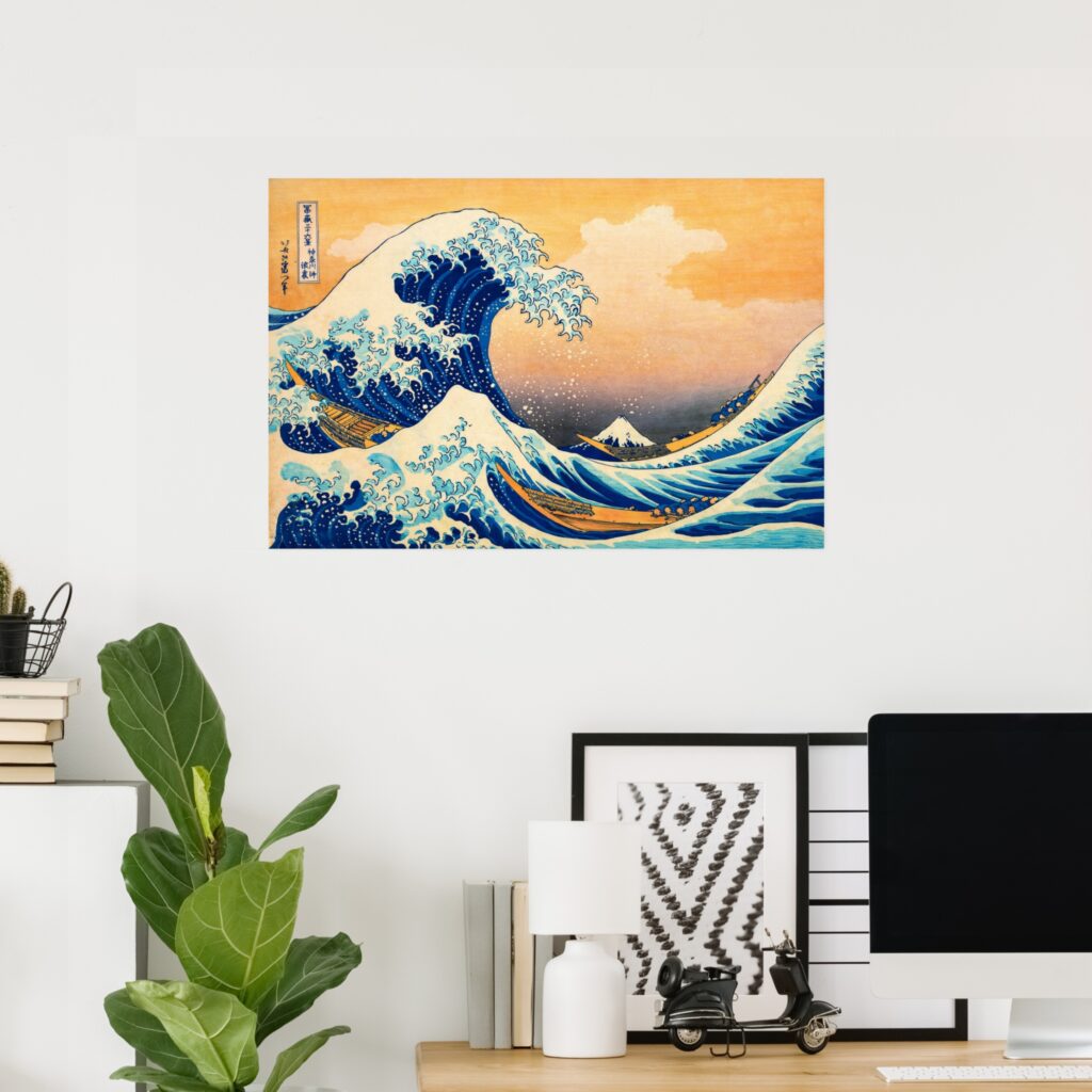 Poster of The Great Wave off Kanagawa by Katsushika Hokusai displayed on a minimalist home office wall above a wooden desk with a computer, framed art, lamp, books, and green plant.