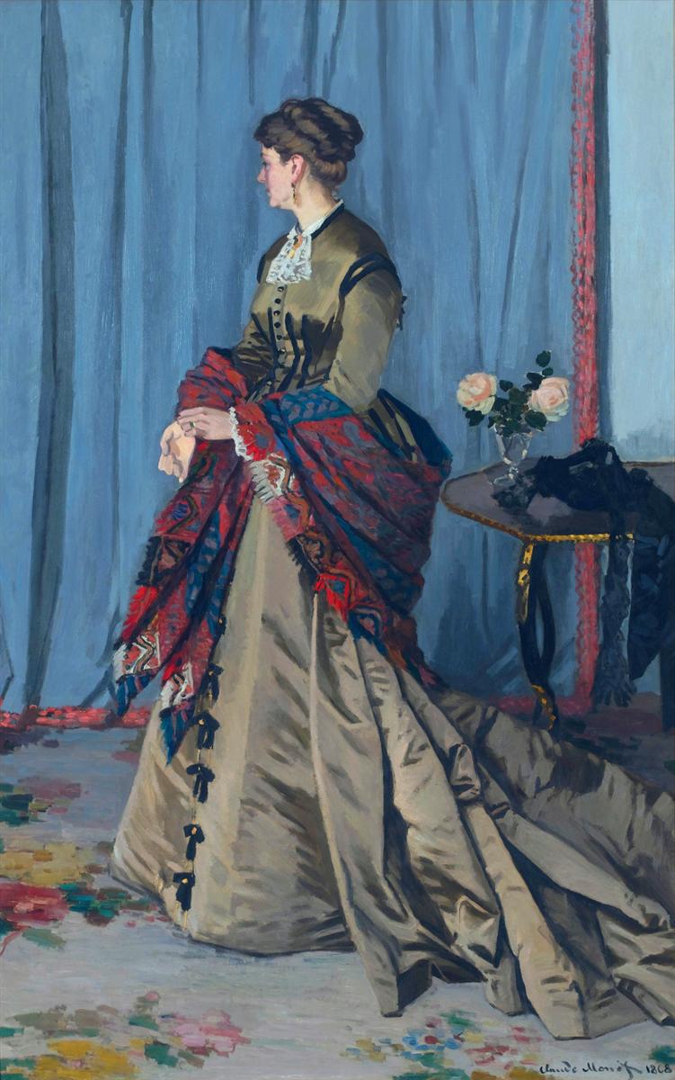 Claude Monet’s Portrait of Madame Gaudibert shows an elegantly dressed woman standing in profile before blue curtains, wearing a pale gown with a long train and a richly colored red and blue shawl, beside a small table with flowers.
